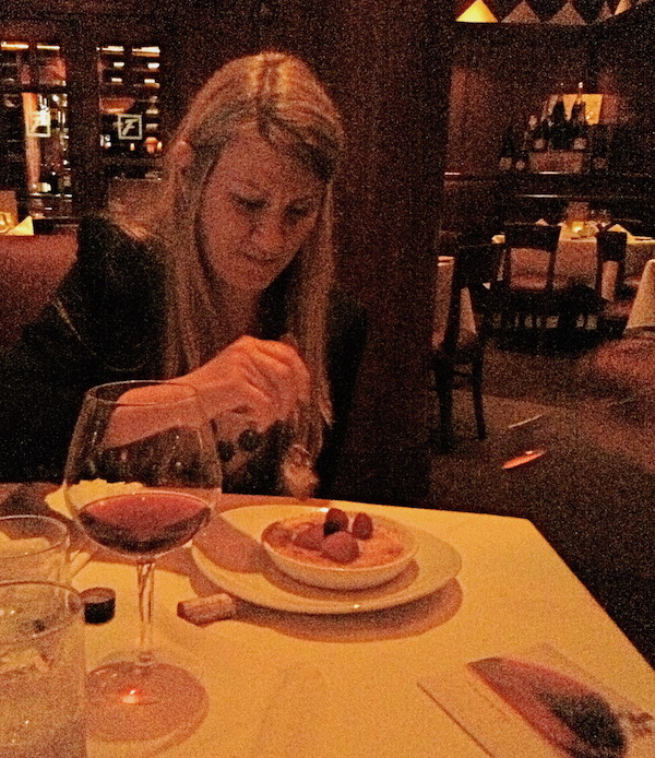 A woman with long blond hair eating a dish of custard topped with berries