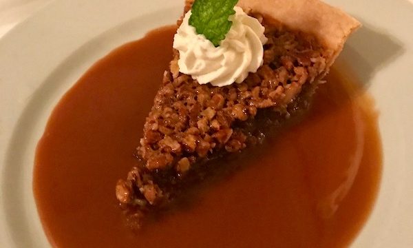 Luscious Pecan Pie with Caramel Sauce and a rosette of whipped cream and mint leaf on a white plate