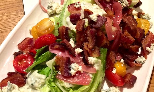 A large white rectangular plate topped with lettuce, tomatoes, bacon and blue cheese crumbles