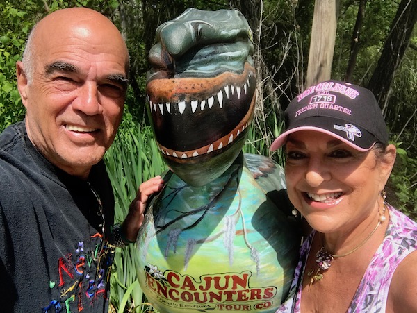 A man in a black t-shirt and a woman in a black and pink ball cap with a fun alligator statue