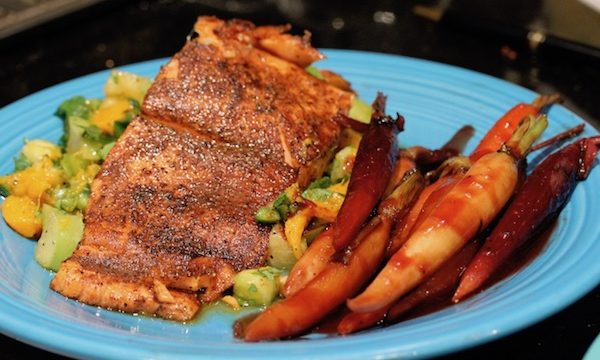 A medium blue dinner plate topped with Garam Masala Dusted Salmon on a Bed of Mango Tomatillo Salsa with Candied Ginger Carrots