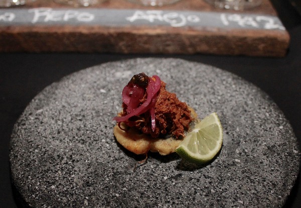 A round grey stone dish topped with Pauncho De Cochinita + Masa + Black Beans + Pickled Red Onion