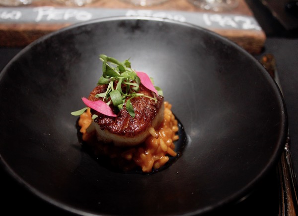A round matte black dish topped with Arroz a la Tumbada + Shrimp Broth + Seared Scallop + Truffle Oil