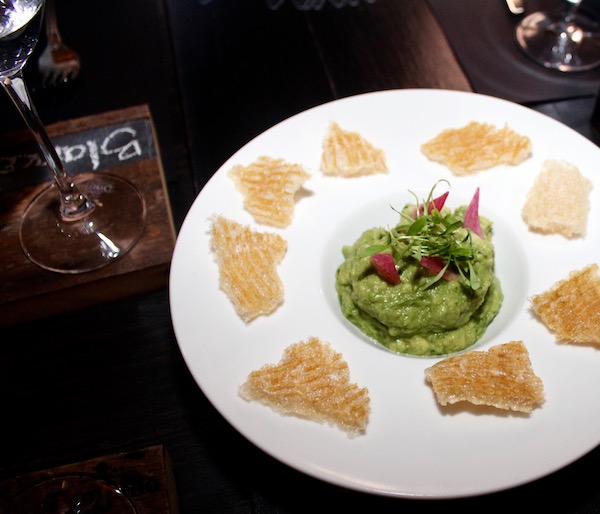A white plate with guacamole in center surrounded by hand made tortilla chips