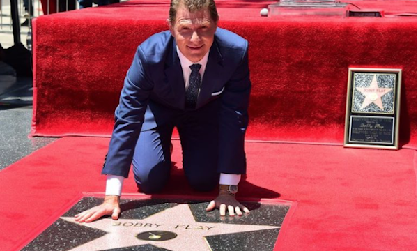 A man in a navy suit kneeling on his Hollywood Walk of Fame Star