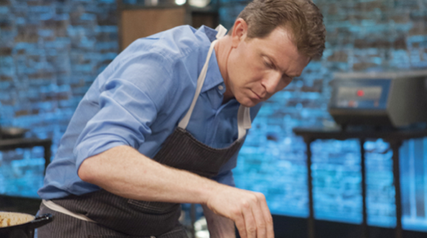 A man with a chef's apron seasoning food.