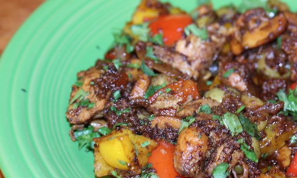A light green dinner plate topped with Chorizo Spiced Chicken Thighs with Peppers Onions Olives and Mushrooms