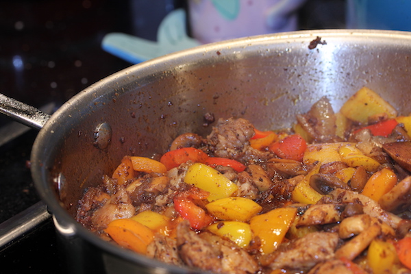 A steel pan filled with peppers, chicken chunks and chorizo
