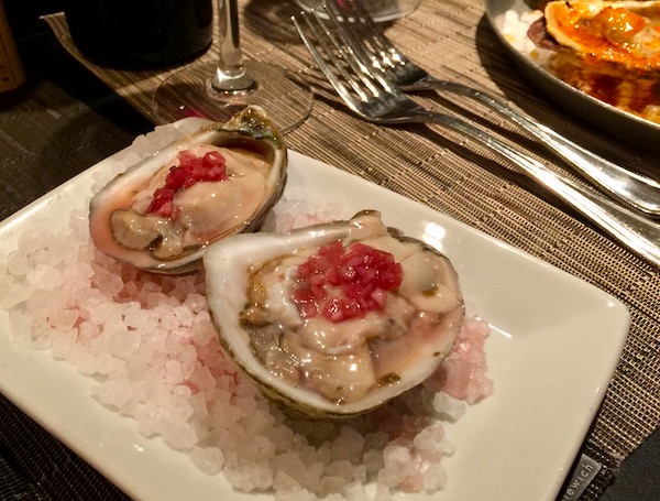 Two Raw Oysters with Sauce Mignonette sitting in rock salt on a white square plate