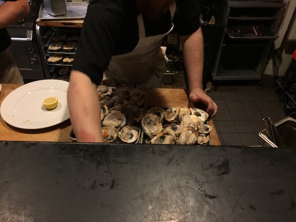 A man in black shirt and apron Prepping Oysters for the Wood Burning Oven