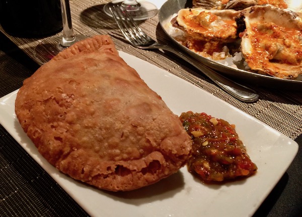 A golden hand pie with chutney on a white rectangular plate
