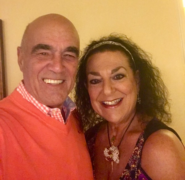 A bald headed man in an orange sweater and a dark haired woman in a paisley dress