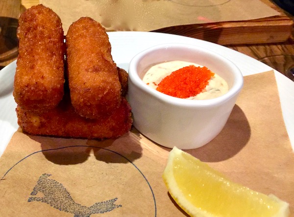 Conch Croquettes on brown paper with a dish of sauce topped with red caviar and a lemon wedge