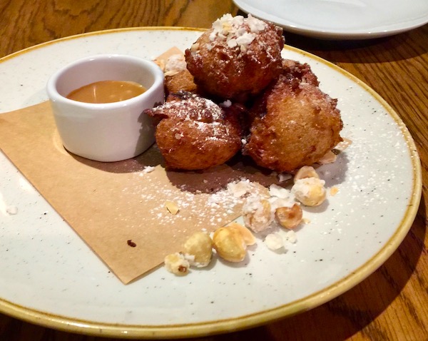 Banana Zeppole with Rum Caramel and Hazelnuts on a beige napkin on a white plate
