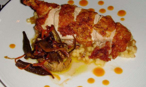 A white dinner plate topped with sliced fried chicken, vegetables and dot of bright orange sauce.