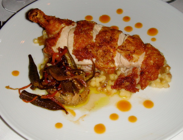 A white dinner plate topped with sliced fried chicken, vegetables and dot of bright orange sauce.