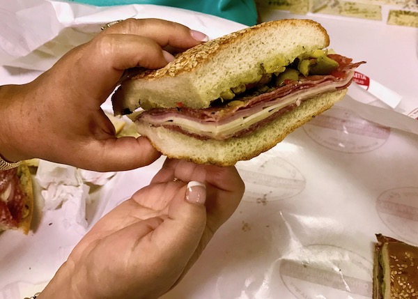 A woman's hands holding a Muffaletta slice at Central Grocery