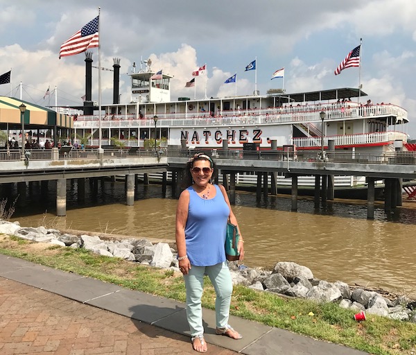A woman Along the Riverwalk with the Natchez river boat behind her