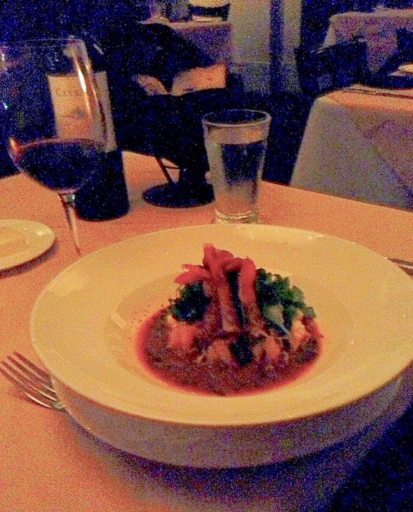 A white bowl filled with shrimp and grits sitting a a table with wine glasses.