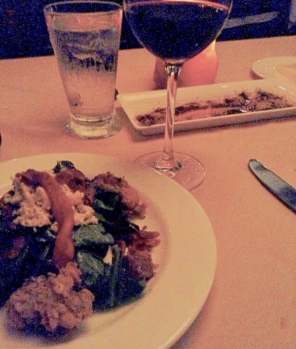 A large white plate with salad greens, roasted pepper strips and fried oysters on a table with a wine glass and utensils.