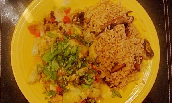 Bright yellow dinner plate on black placemat with tilapia filet, vegetables, brown rice and mushrooms