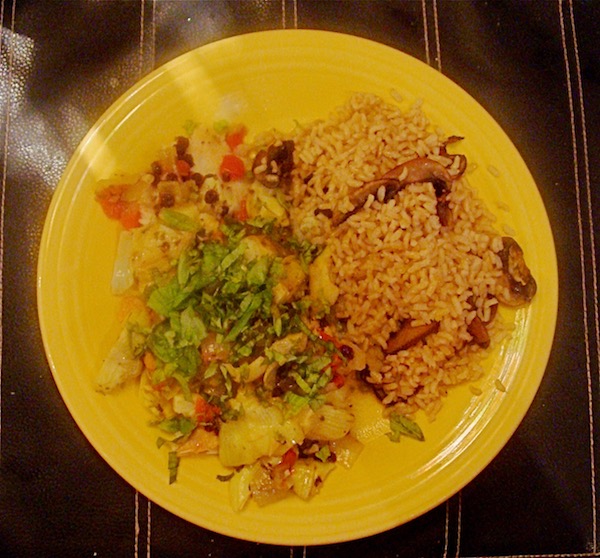 Bright yellow dinner plate on black placemat with tilapia filet, vegetables, brown rice and mushrooms