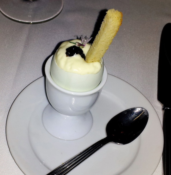 A small white plate holding an egg cup filled with a mousse, caviar and a bread stick