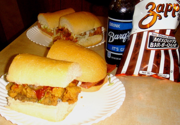 White plates topped with Po' Boy sandwiches, a bottle of Barq's root beer and a bag of chips