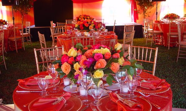 A large tent draped in orange irridescent fabric, round tables and chairs with the same tablecloths and floral centerpieces