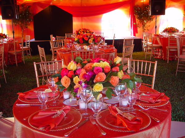 A large tent draped in orange irridescent fabric, round tables and chairs with the same tablecloths and floral centerpieces