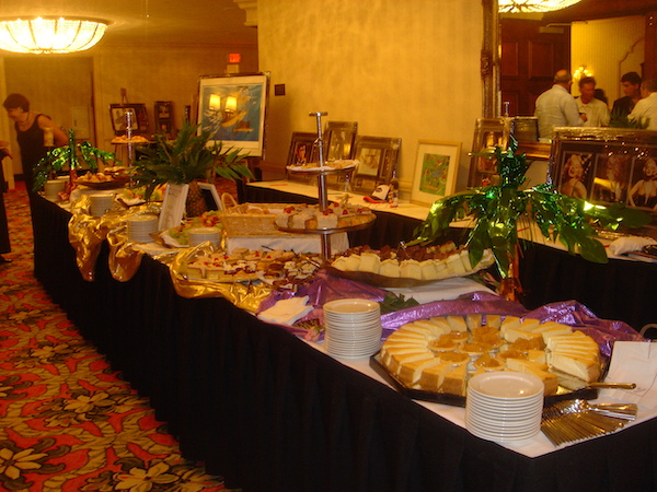 A long buffet table with white top and black skirting complete cover with food and plates.