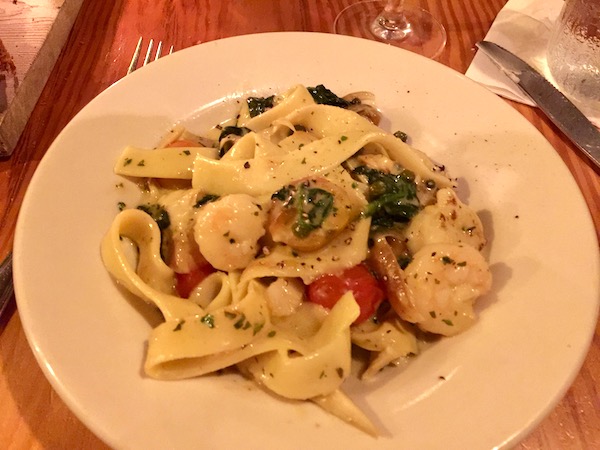 A white pasta dish filled with pasta, shrimp, tomatoes and parsley