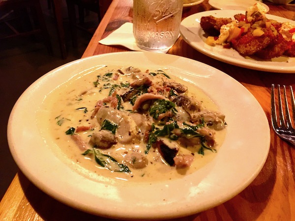A white shallow soup bowl filled with oysters, soup and lots of sliced mushrooms