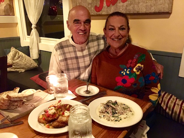A man and a woman seated at a table in a restaurant with plates of food on the table in front of them.