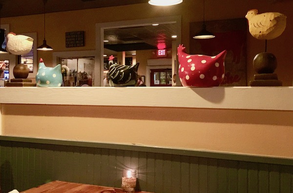 A privacy wall at a restaurant topped with several ceramic hens in various colors