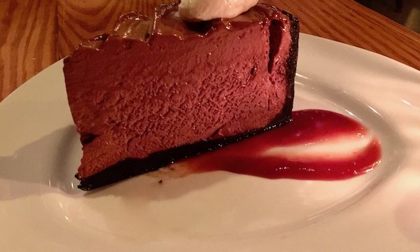 A white plate with a raspberry swoosh topped with a tall wedge of chocolate pie