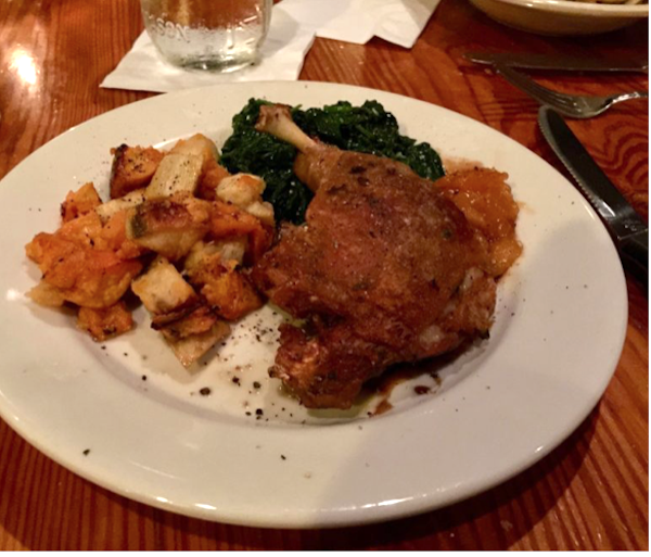 A white plate with a duck leg and thigh vegetables and greens