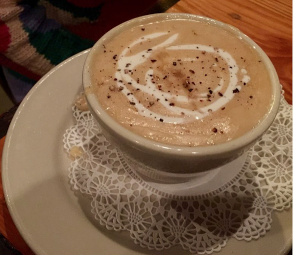 A small soup cup on a plate with a doily. Filling the bowl is creamy crab soup with a white swirl.