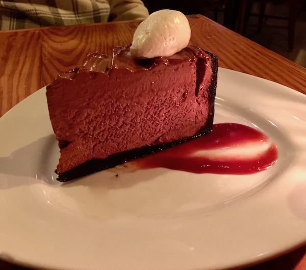 A white plate with a raspberry swoosh topped with a tall wedge of chocolate pie