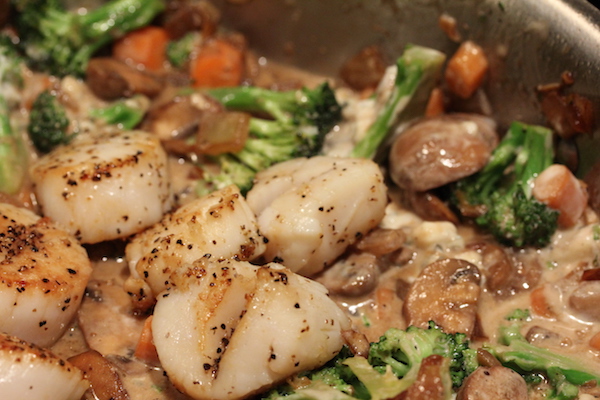 An anodized pan with scallops, broccoli and carrots cooking in it.
