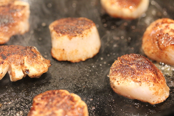 An anodized pan with well seasoned scallops searing in it.