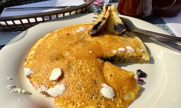 A stack of blueberry pancakes with small pieces of melting butter on a white plate