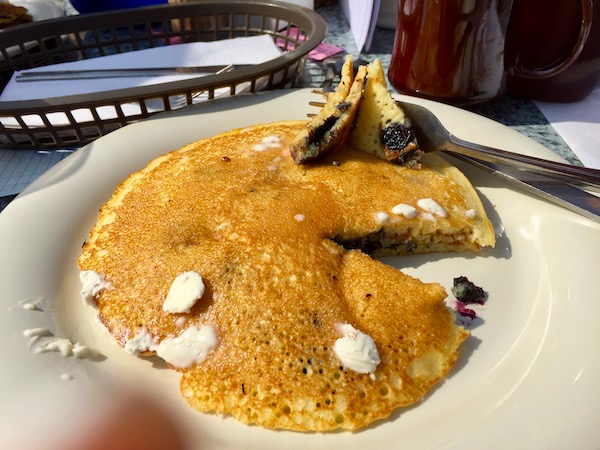 A stack of blueberry pancakes with small pieces of melting butter on a white plate