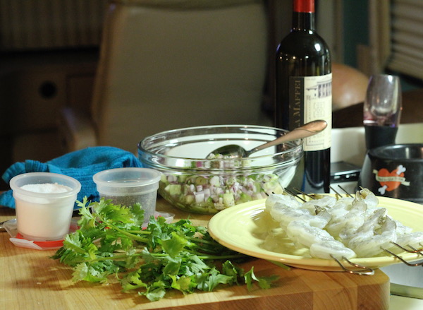 An assemblage of ingredients, bowls, plates with shrimp skewers and a bottle of wine