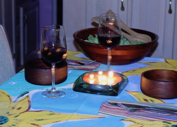 A table set with colorful tablecloth, salad bowls, wine glasses filled with red wine and candles.