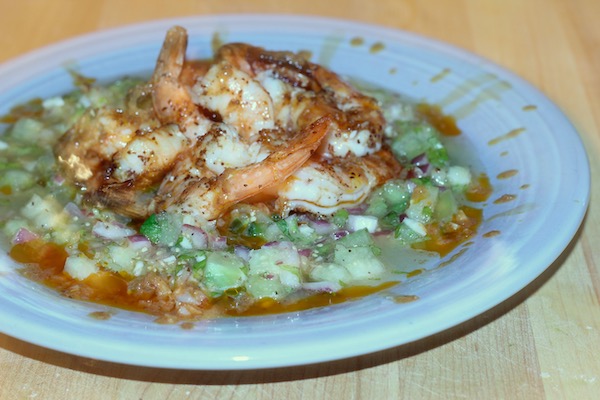 A light blue dinner plate topped with Grilled Shrimp Brushed with Smoked Chile Butter on a Bed of Tomatillo Salsa