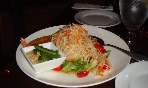 A white plate with green papaya salad on a black tablecloth