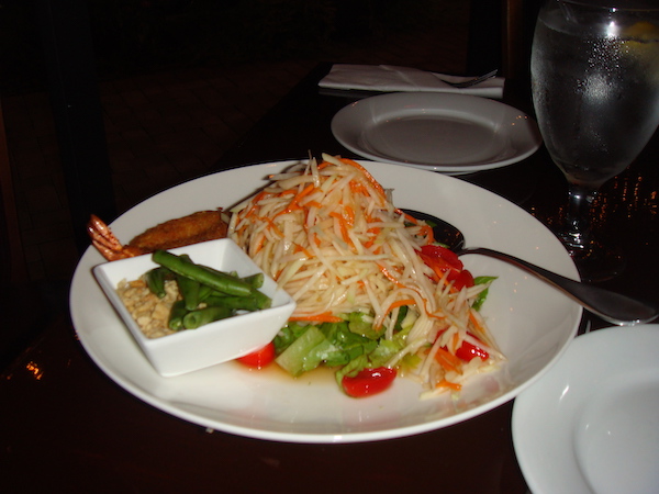 A white plate with green papaya salad on a black tablecloth