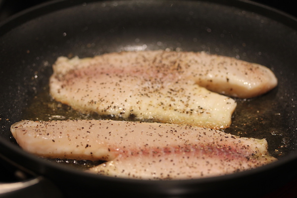 Anodized sauté pan with two tilapia filets cooking