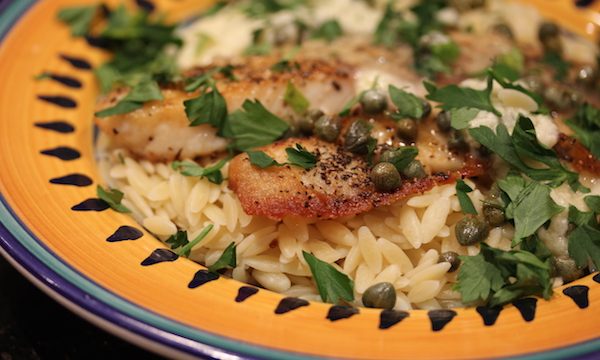Yellow and blue rimmed pasta bowl with orzo, pan cooked tilapia, capers and parsley